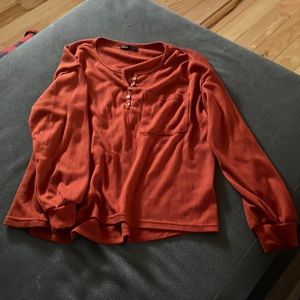 Burnt orange long sleeve top with buttons on the top and a small pocket